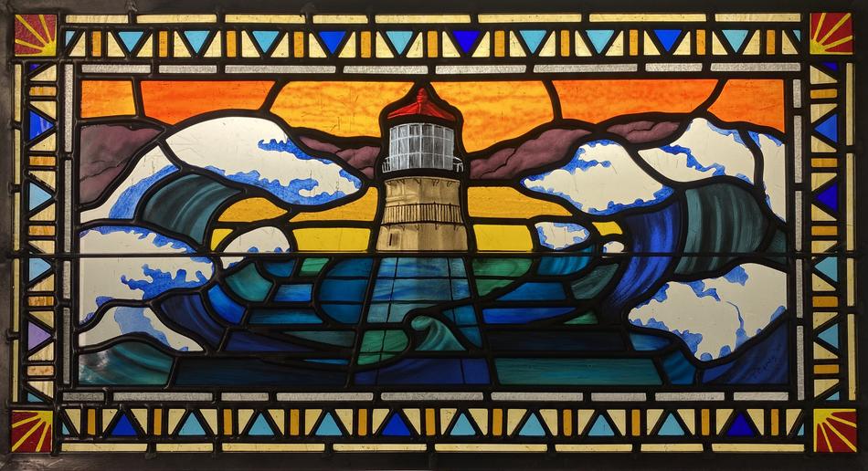 Painted stained glass window depicting a lighthouse and crashing waves at sunset with geometric border