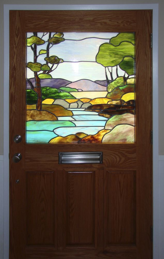 Custom stained glass entry door depicting a river, mountains, and trees landscape scene