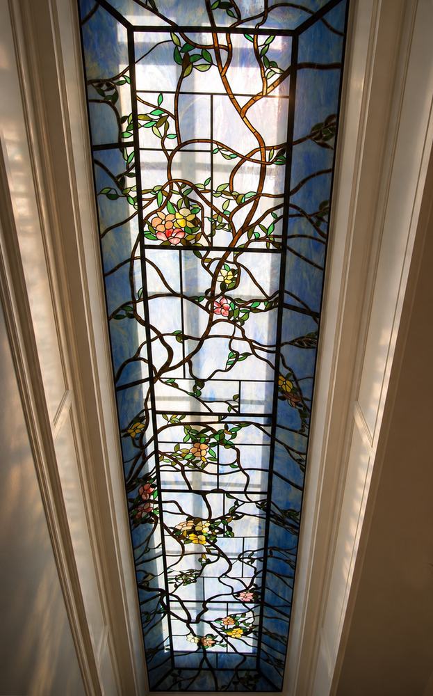 Tall custom stained glass skylight panel with flowering vine design in blue and green tones