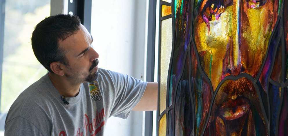 Tim Carey examining a painted stained glass panel in his studio